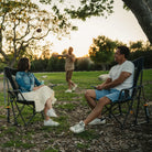 A couple sitting together at a park in their Comfort Pro Rockers as they watch someone throw a football. 