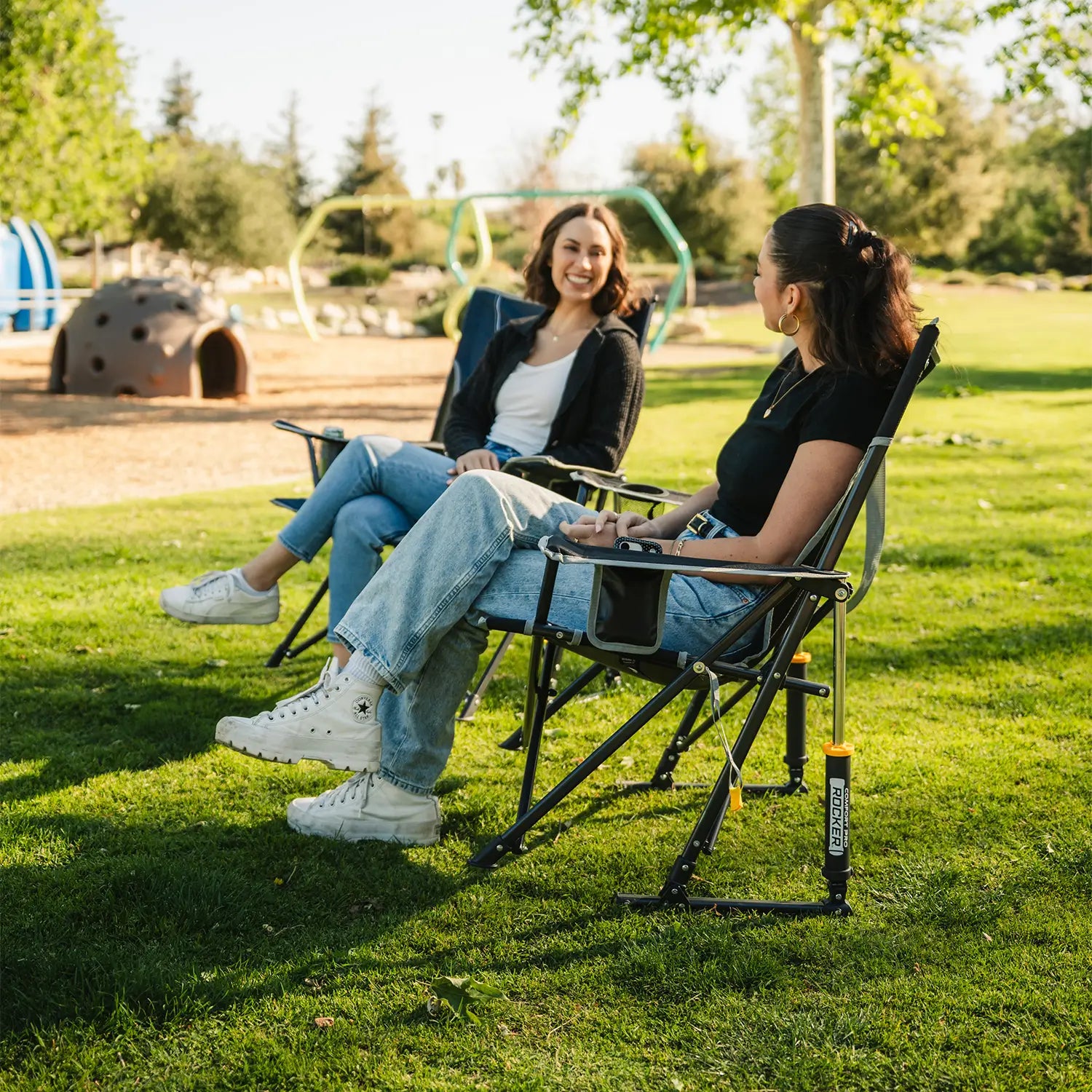 A woman sitting in a black Comfort Pro Rocker chair talking to another woman sitting in an Eazy Chair. 