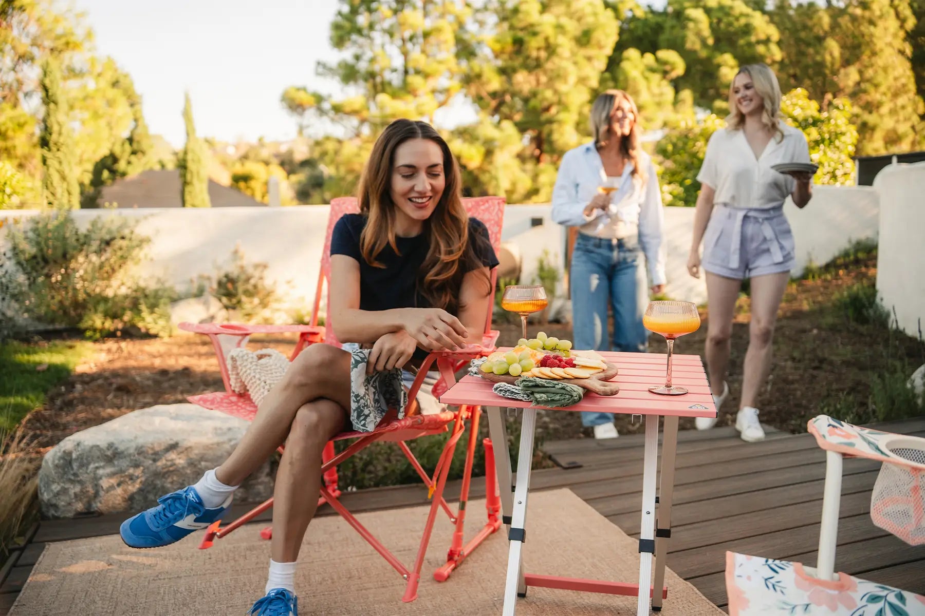 A woman reaching for a snack resting on a coral Compact Table as the woman sits in a coral Comfort Pro Rocker. 