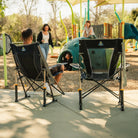 A man sitting in a Comfort Pro Rocker Chair watching his children play on a playground. 