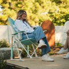 Woman smiling while seated in a pastel green Comfort Pro Rocker at a social outdoor event.