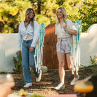 Two women carrying pastel green Comfort Pro Rockers to a backyard on their shoulder.