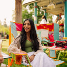 A woman smiling while sitting in a sweet tea comfort pro rocker at an outdoor event. She is wearing a beige knit cardigan over a green top and a white skirt.