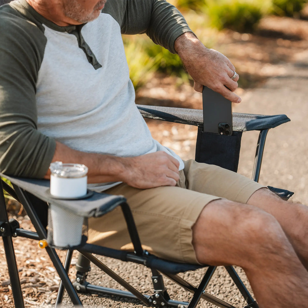 Man relaxing in the Heathered Charcoal Comfort Pro Rocker XL chair, placing a phone in the side pocket.