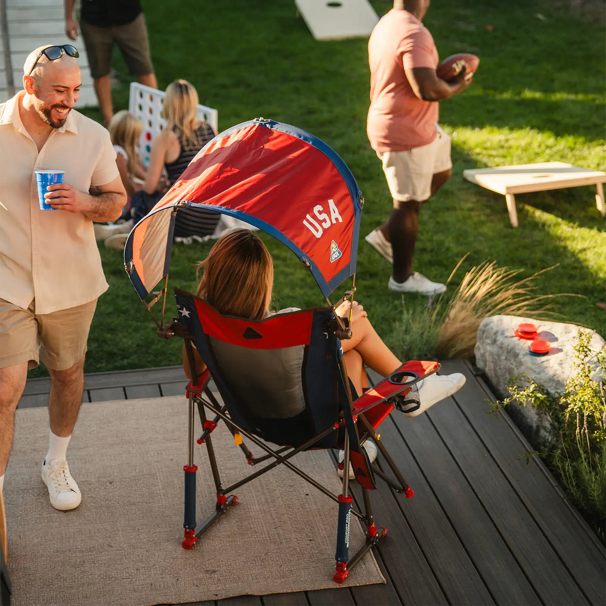The backside of a Comfort Pro Rocker chair with a USA Sunshade Accessory attached while a woman sits in the chair. 