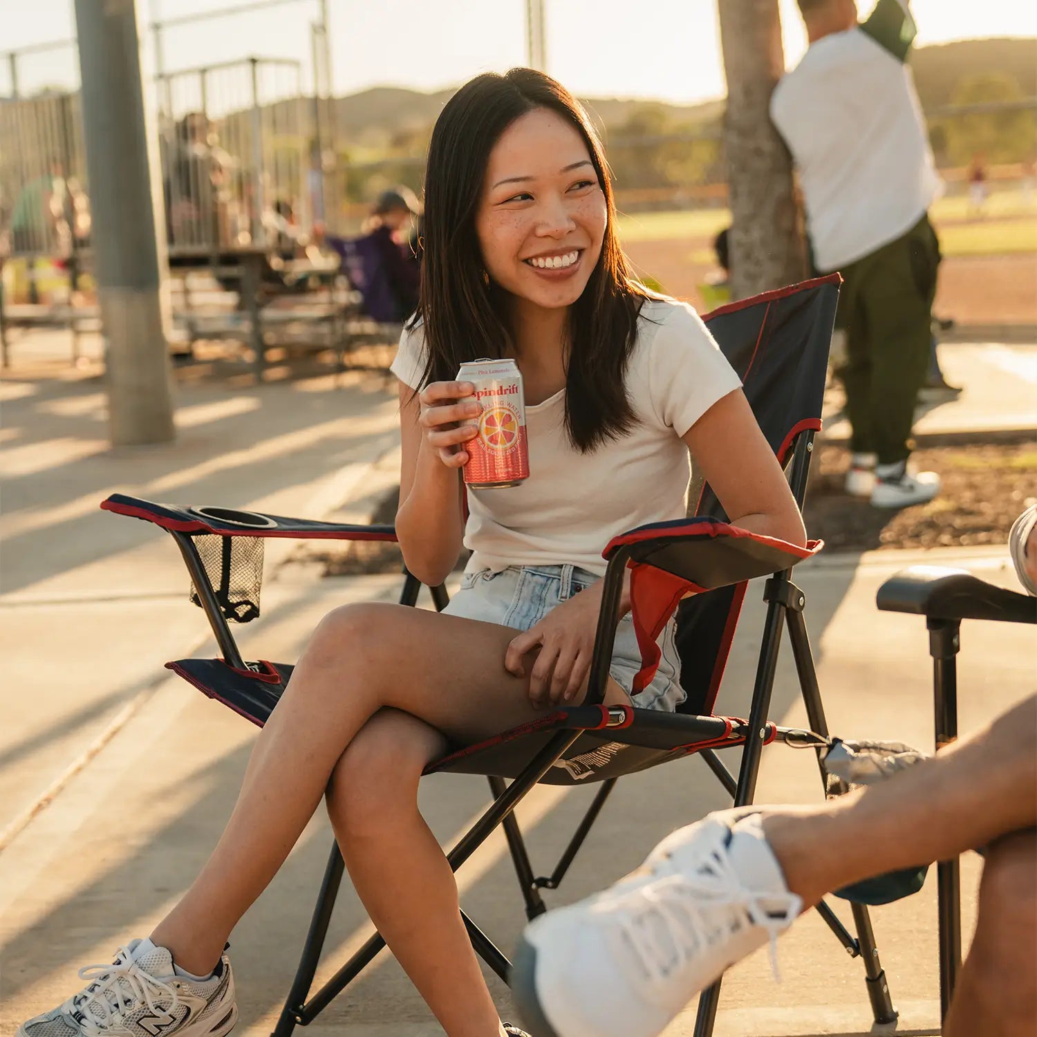 A woman sipping on a can of soda as she sits in an indigo/red Comfort Quad Chair. 