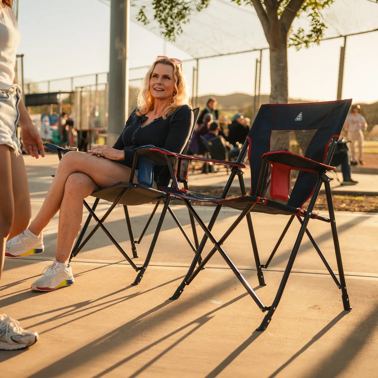 A woman walking towards an indigo/red Comfort Quad Chair to sit in. 