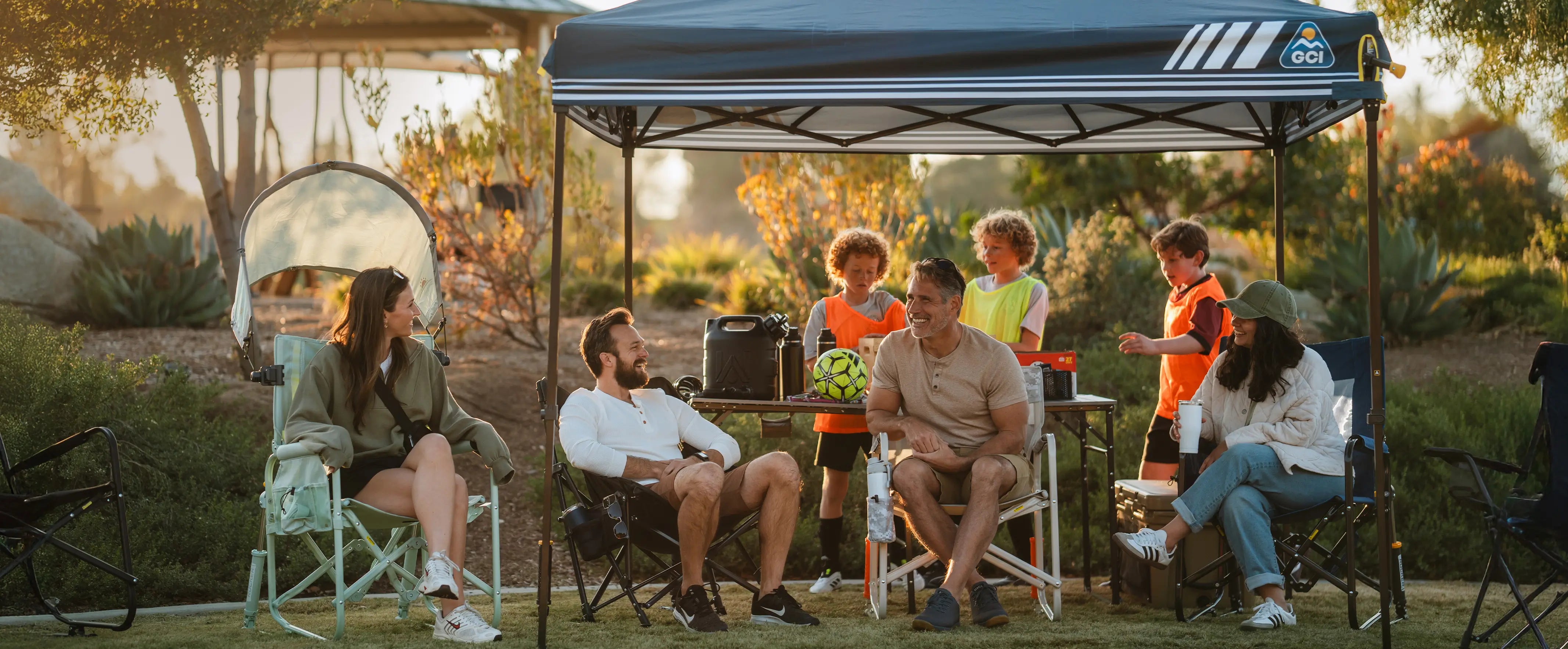 A group of parents and kids gather under a LevrUp Canopy at a soccer game, enjoying the shade and comfort of their SunShade Rocker, Freestyle Rocker, and Compact Camp Chair. The setup provides the perfect sideline retreat for game-day relaxation.