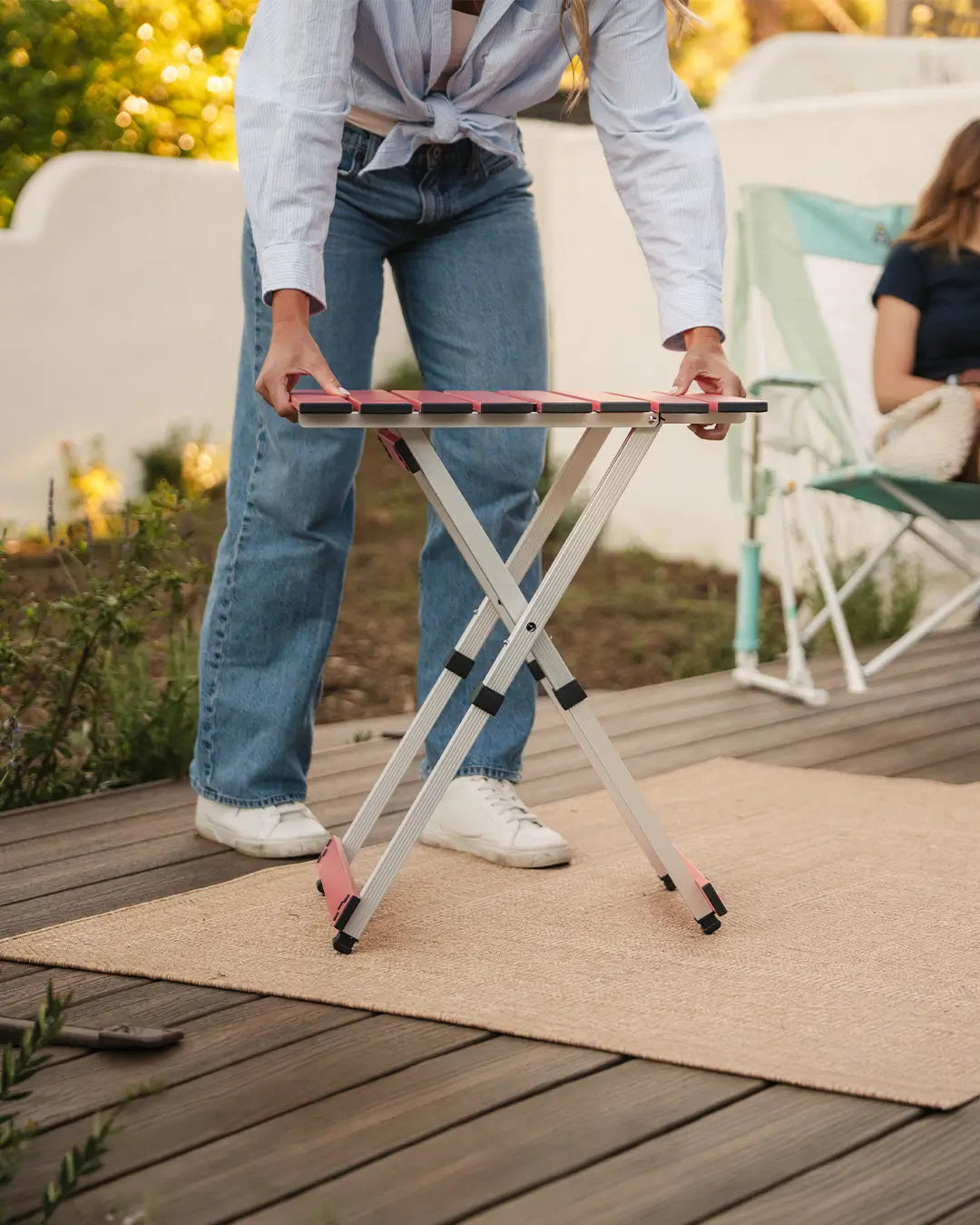 A woman setting up a coral compact camp table 20 in a backyard setting. 