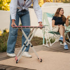 A woman putting the coral Compact Camp Table next to a group of people sitting in rockers. 