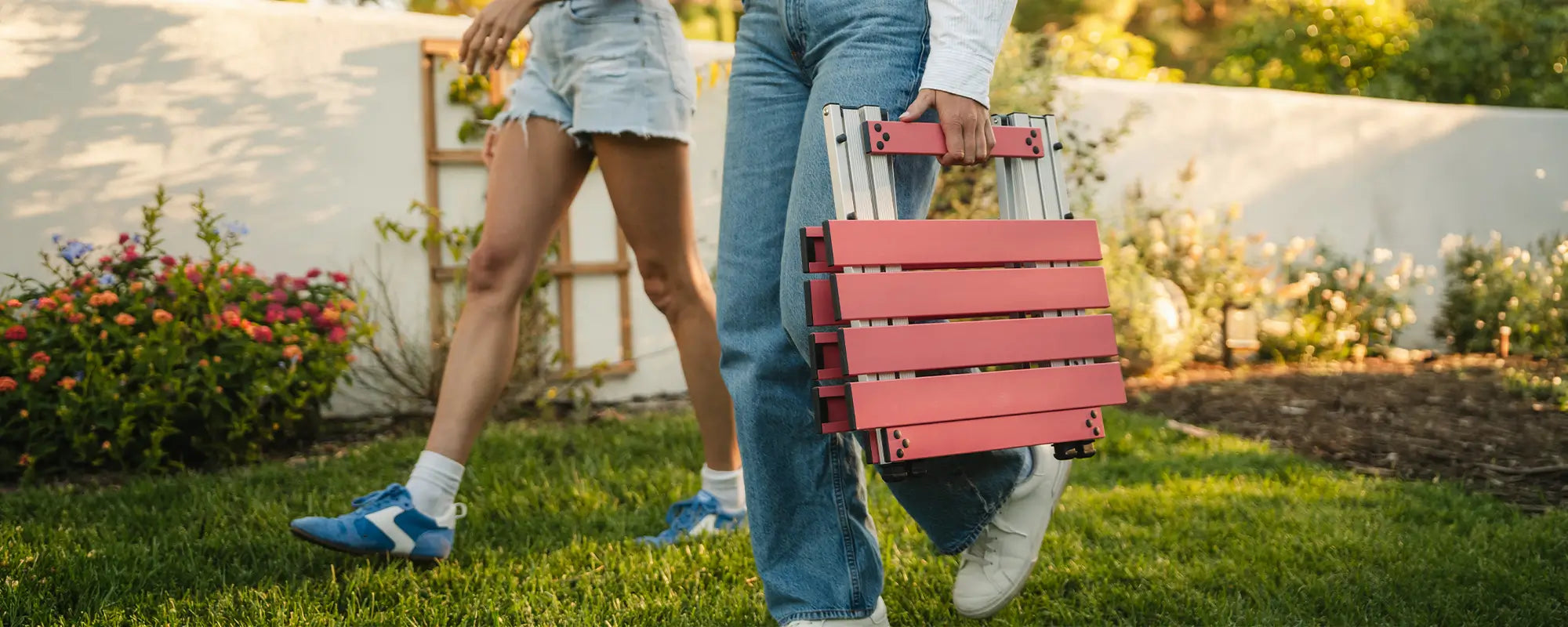 A woman carrying a coral Compact Camp Table to a backyard event. 