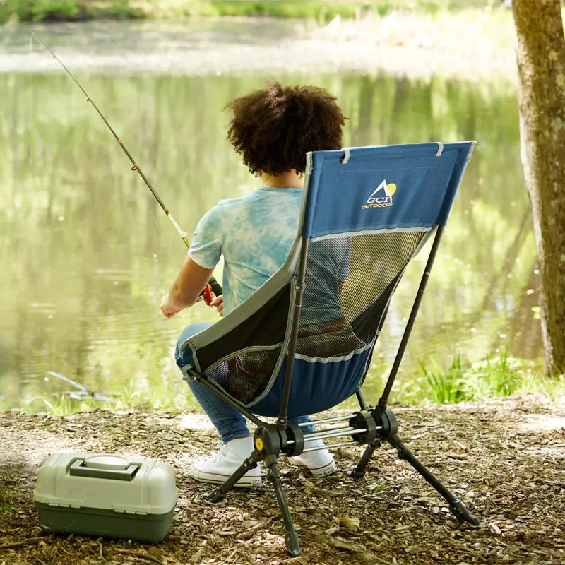 A person sitting in an indigo Compack Rocker and fishing in a pond. 