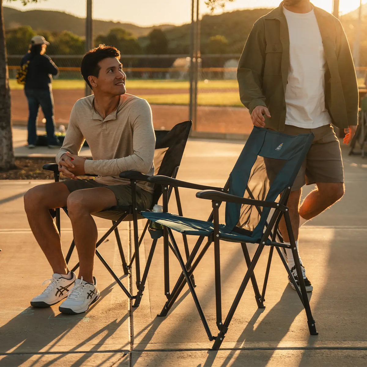 A person walking towards an empty Eazy Chair seat while another person sits next to the chair beside him. 