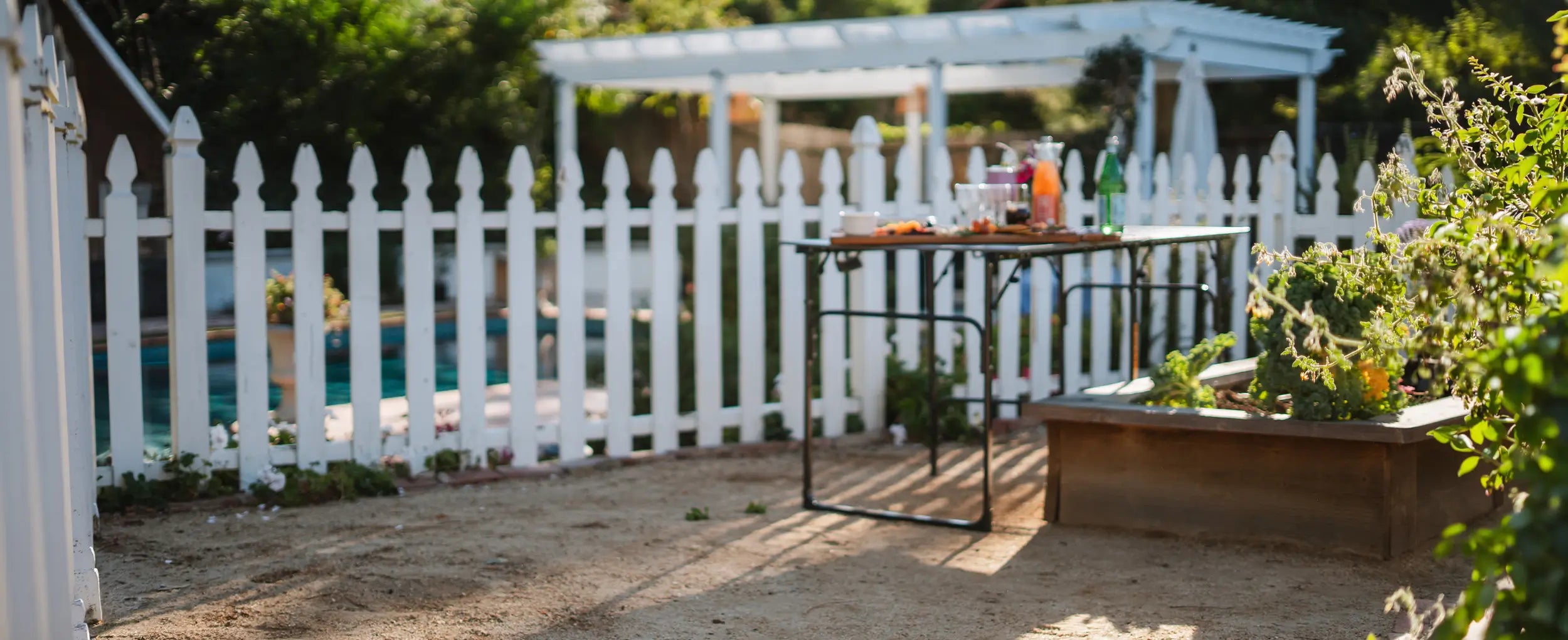 A slim-fold table positioned next to a pool and garden bed. 