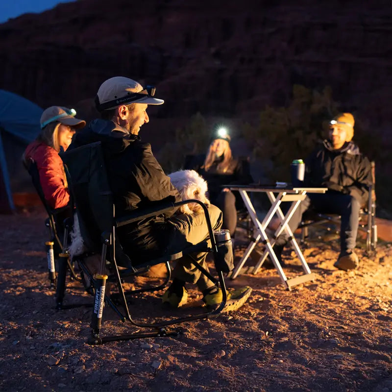 Group of campers gathered around a fire, seated in Firepit Rockers with headlamps and warm gear, enjoying the evening outdoors.