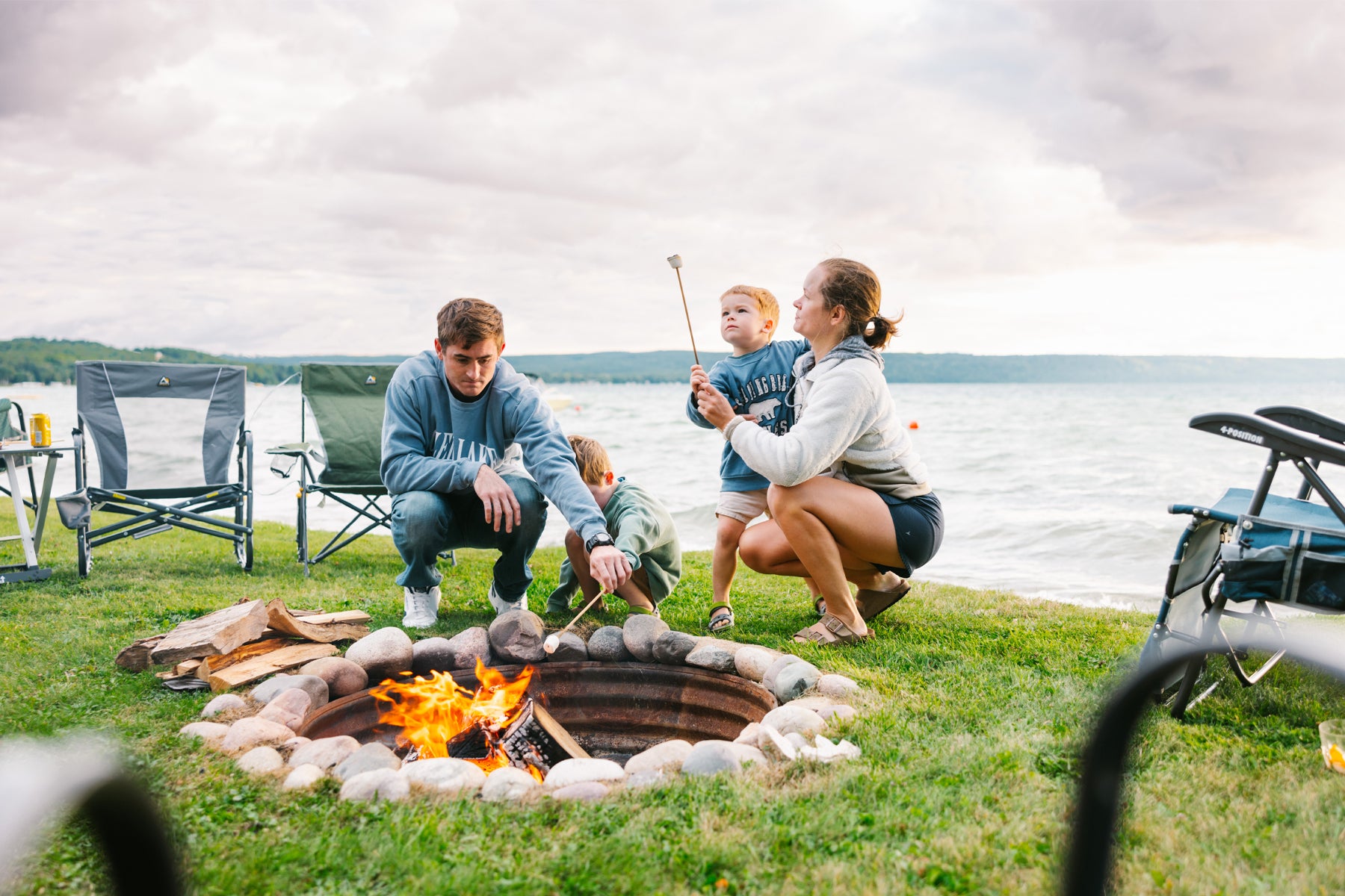 Person sitting in a GCI Firepit Rocker by a firepit at a campsite, roasting marshmallows.