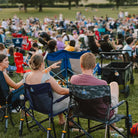 Two concert goers sitting in freestyle rocker elite chairs at a venue.