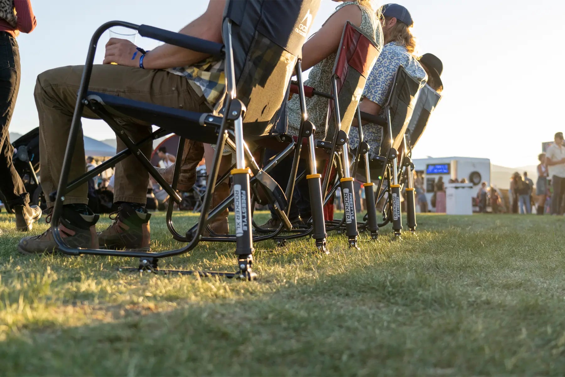 Row of Freestyle Rocker chairs at an outdoor event. People are seated comfortably on the grass with drinks in hand.