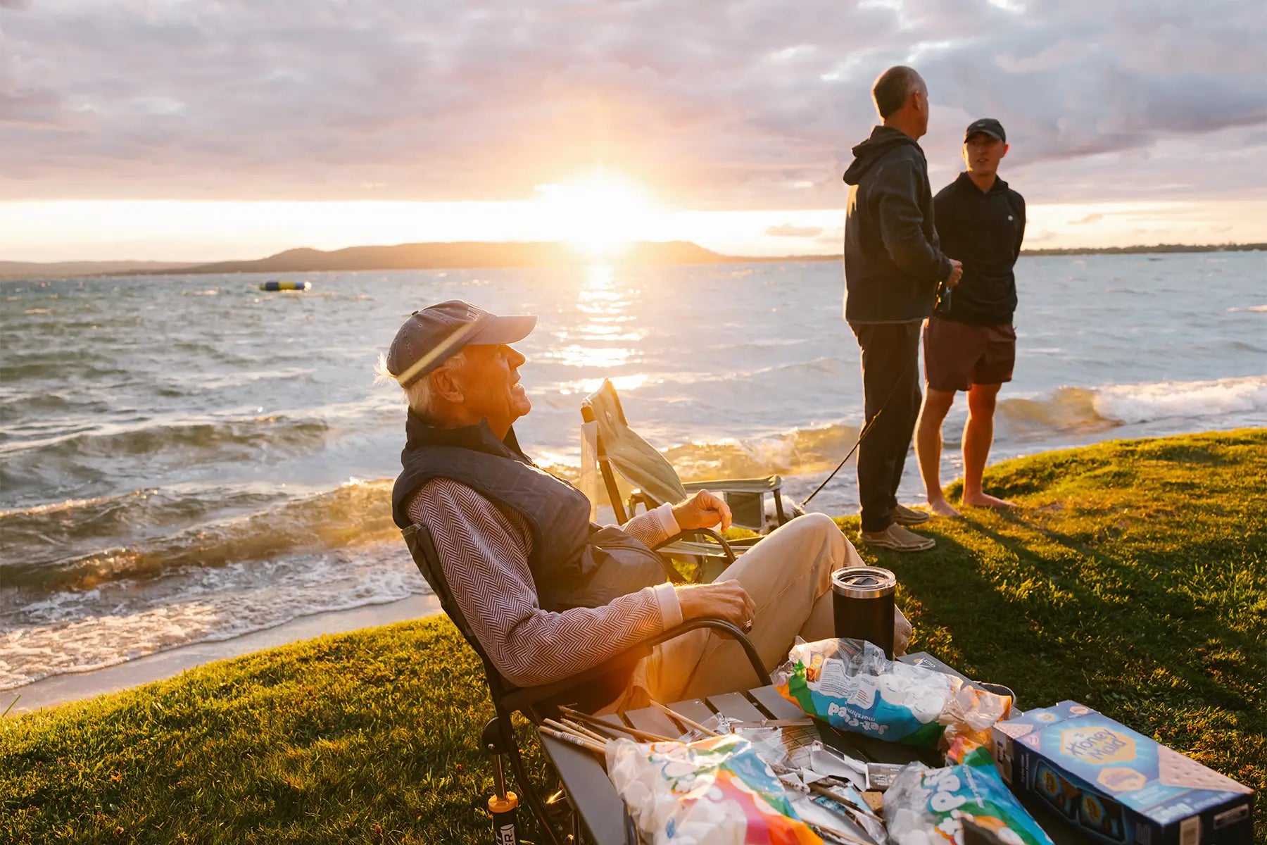 An older man sitting in a Freestyle Rocker chair while a group of people cook smores. 