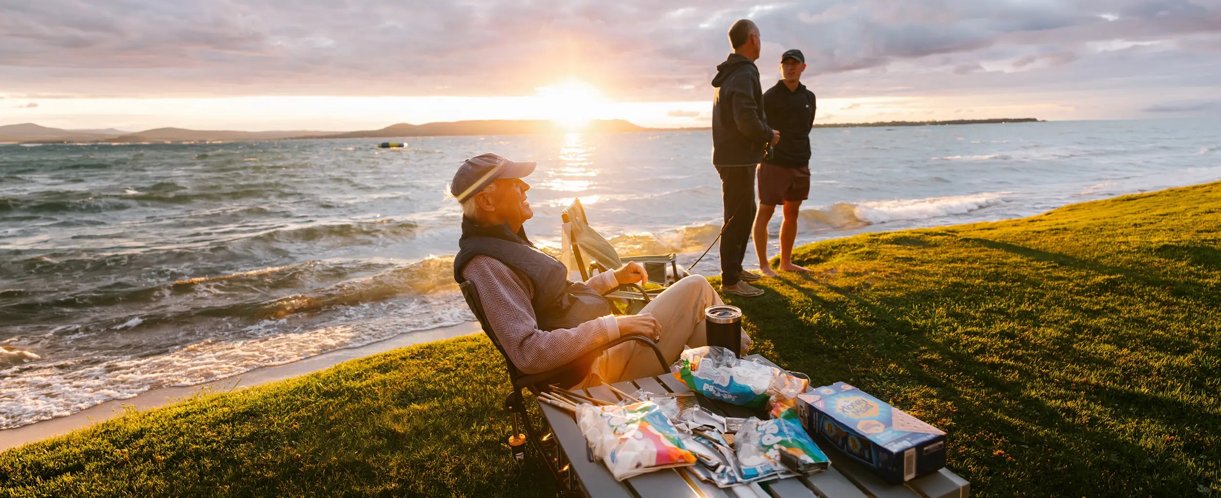 An older man sitting in a Freestyle Rocker chair while a group of people cook smores. 