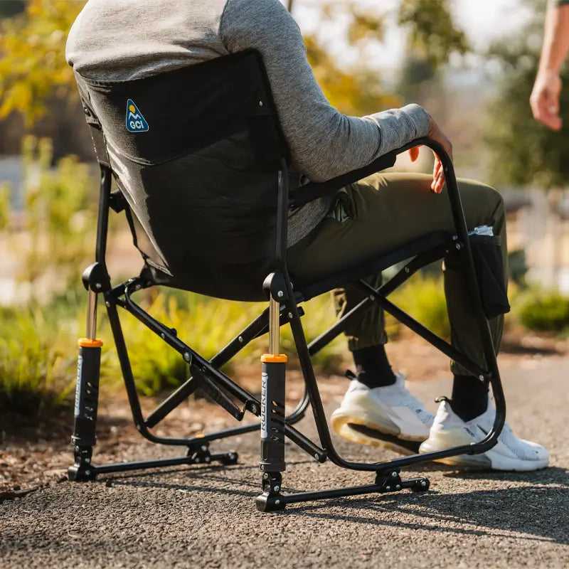 Man seated in a black Freestyle Rocker Elite chair, showing dual spring-action shocks and sturdy frame on a paved outdoor path.
