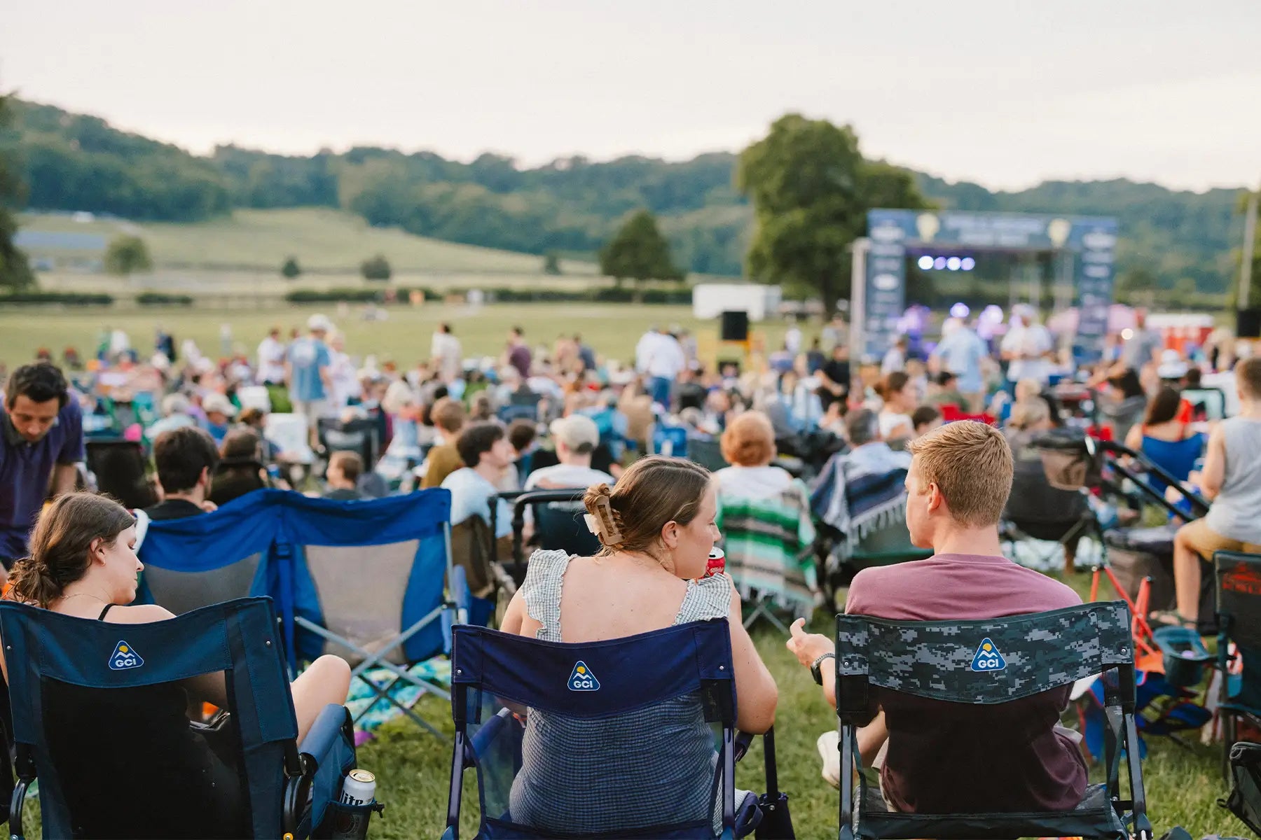 A group of concert goers sitting in gci outdoor chairs while watching an artist perform. 