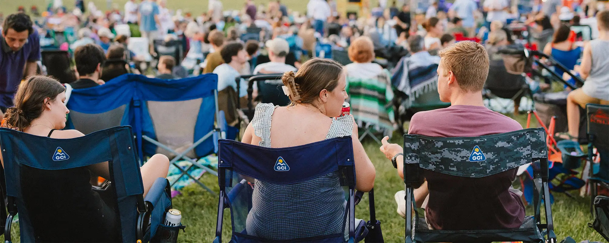 A group of concert goers sitting in gci outdoor chairs while watching an artist perform. 