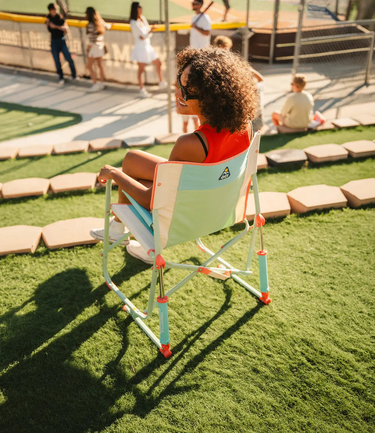 A woman sitting in an ivory Freestyle Rocker while attending a baseball game. 