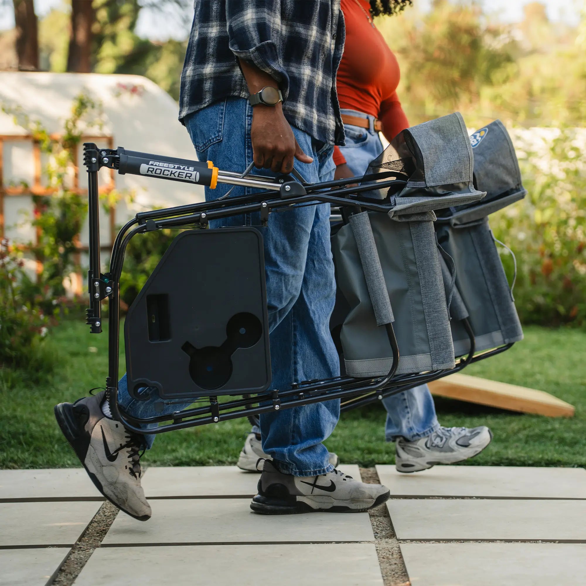 Two people carrying their freestyle rocker with side table by using the integrated carry handle. 