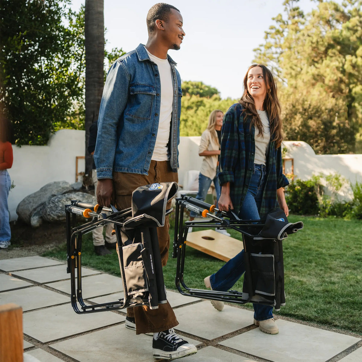 Two people carrying a black freestyle rocker xl through a backyard by using the integrated carry handle. 