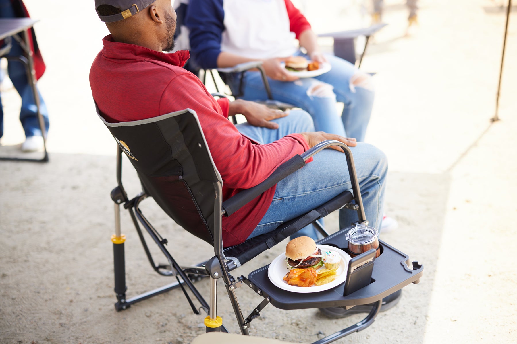 A man sits in a Freestyle Rocker XL with a side table holding food and a drink, showing the chair's convenience for meals.