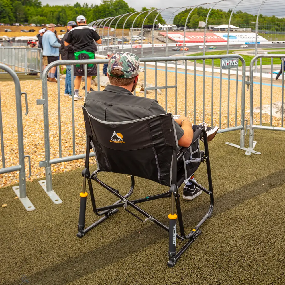 A man watching cars race on a track while sitting in a black Freestyle Rocker XL chair. 