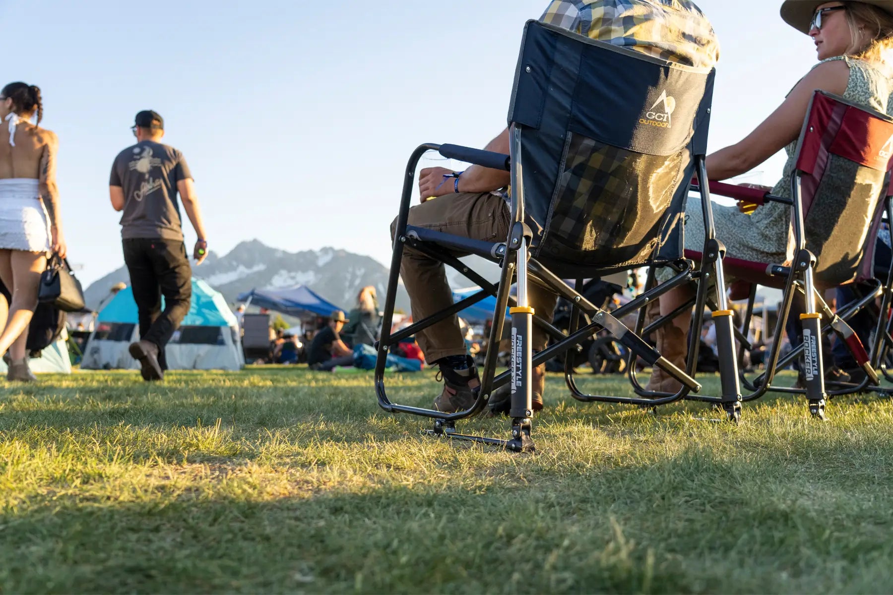 Person reclining in a GCI Freestyle Rocker XL with a side table holding a plate and drink at a park.