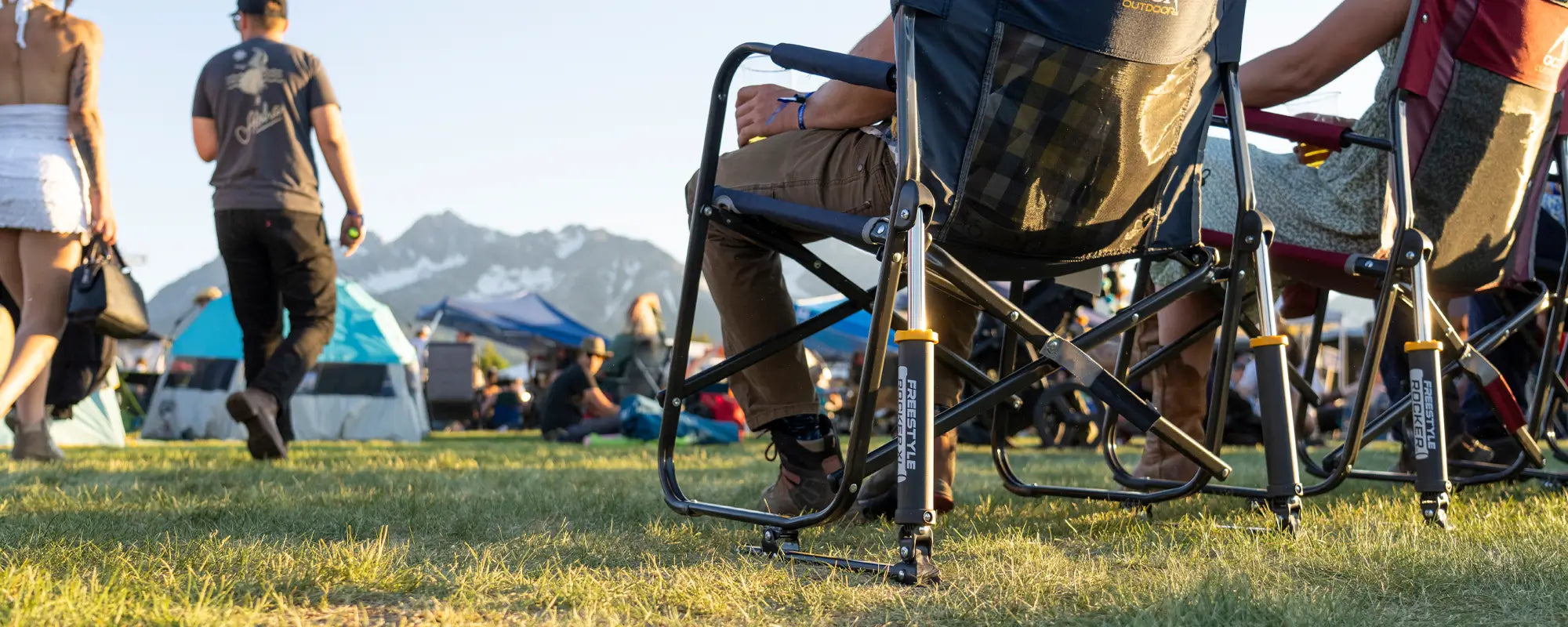 Person reclining in a GCI Freestyle Rocker XL with a side table holding a plate and drink at a park.