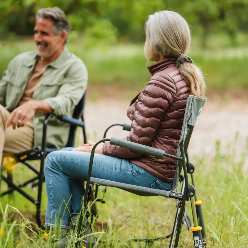 Woman seated in a heathered pewter Freestyle Rocker with Side Table, chatting with a man in a grassy outdoor setting.