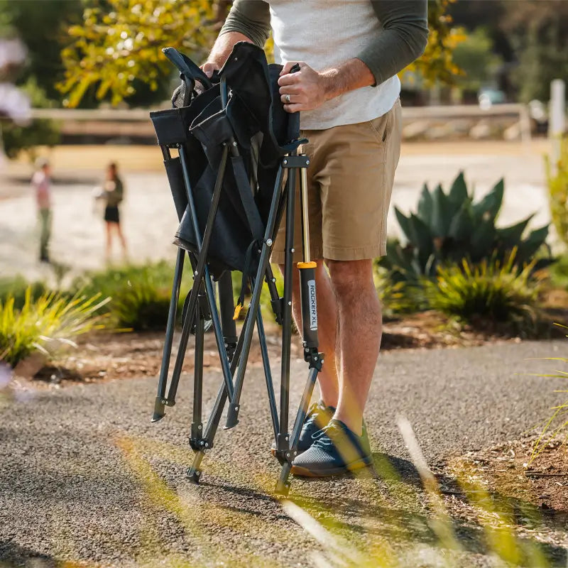 A man folds up a Comfort Pro Rocker XL, showcasing its compact and portable design. The oversized rocking chair collapses easily for convenient transport and storage, making it perfect for outdoor adventures.