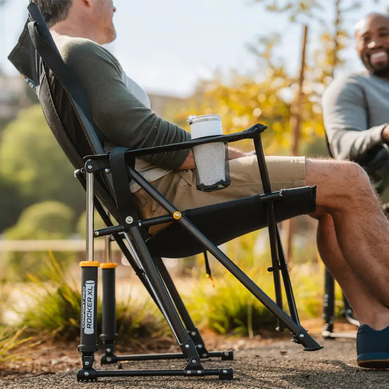 A man relaxes in a Comfort Pro Rocker XL, enjoying the smooth rocking motion. The chair's spring-action rocking technology and sturdy frame provide ultimate comfort for outdoor lounging.