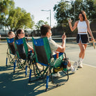 Three people sitting in a pickleball stowaway rocker while a woman high fives a man sitting. 