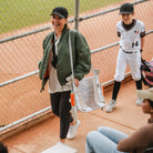 Woman carries a camo GCI Outdoor Stadium Rock-Cliner with orange armrests near a baseball field, highlighting its portability.