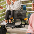 Black GCI Outdoor Stadium Rock-Cliner with gold armrests on a bleacher, highlighting its foldable, rocking stadium seat.