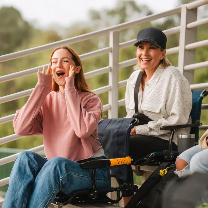 Two women cheering while sitting in her stadium rock-cliner in a bleacher stand.