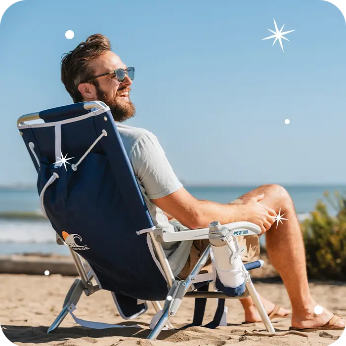 A man sitting on the beach in a backpack beach chair. 