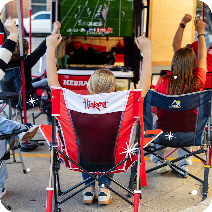 A group of tailgaters sitting watching a football game while sitting in collegiate licensed rocking chairs. 