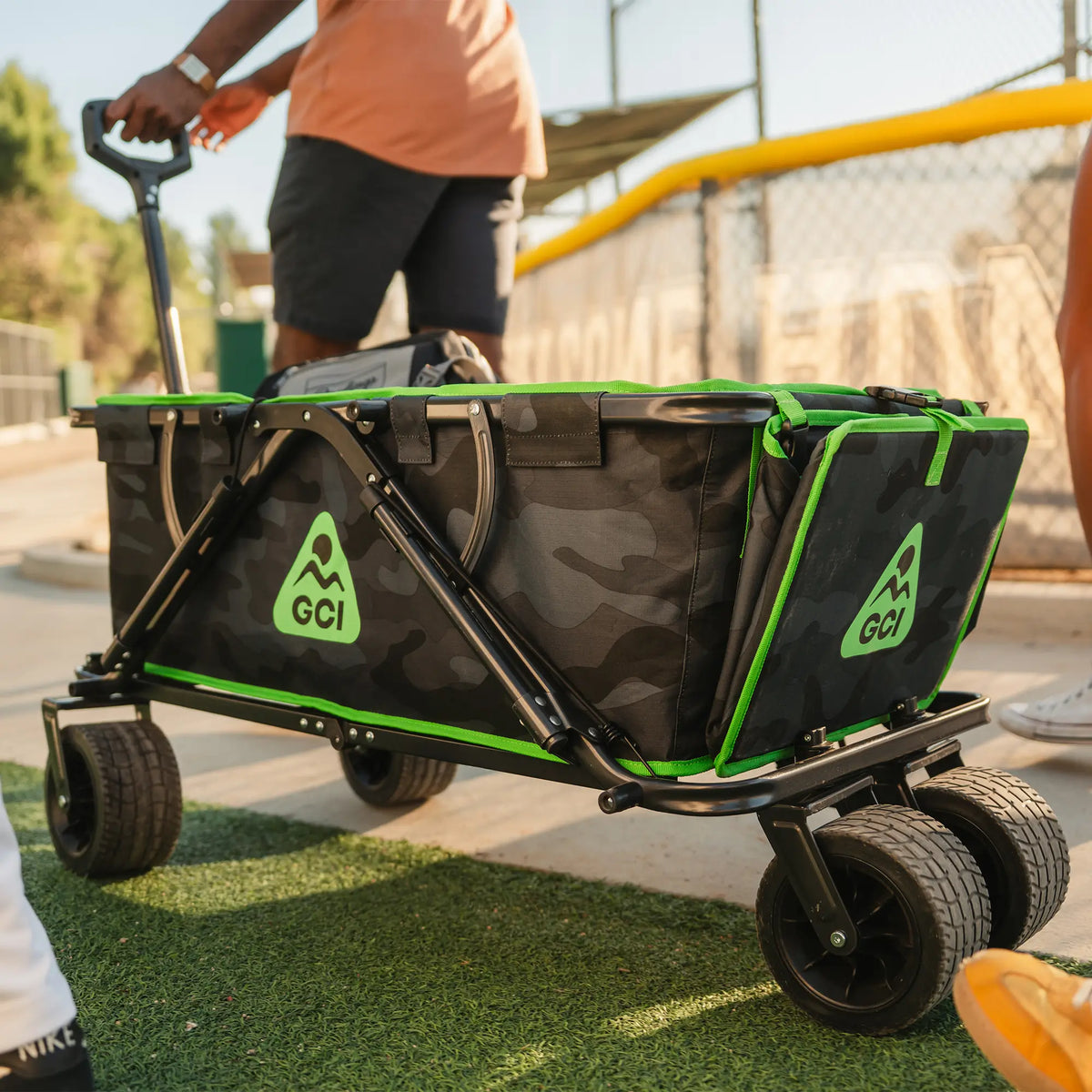 A man pulling a camo Go-Hauler near a baseball field that's loaded with baseball gear. 