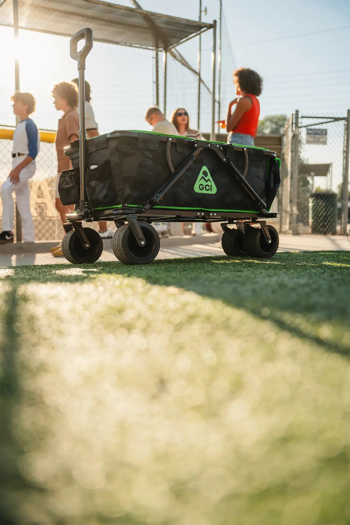 The camo Go-Hauler parked near a group of children baseball players huddled next to a baseball field. 