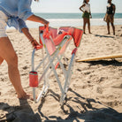 A woman unfolding the coral Grab and Go Rocker on a beach. 
