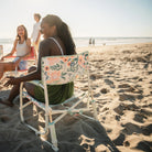 A woman sitting with a group on a beach while relaxing in a floral bouqet Grab and Go Rocker. 