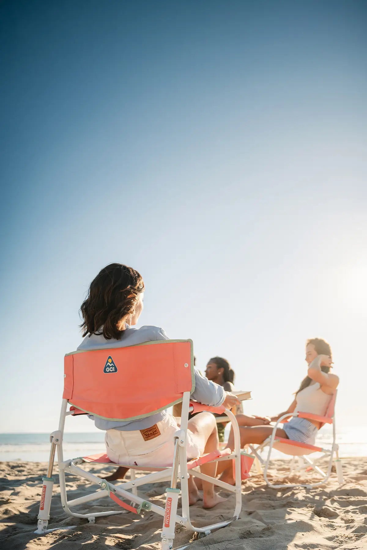 A group of women sitting in GCI Outdoor beach chairs on the coast. 