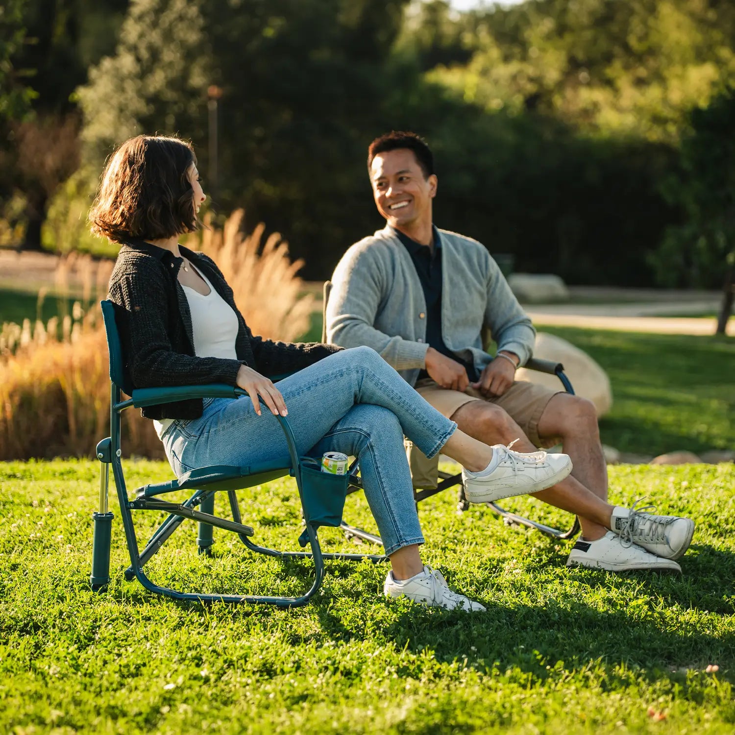 A couple sitting in Grab and Go Rockers while laughing at a park. 