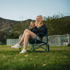 A woman clapping and sitting in a teal Grab & Go Rocker in a grassy area. 